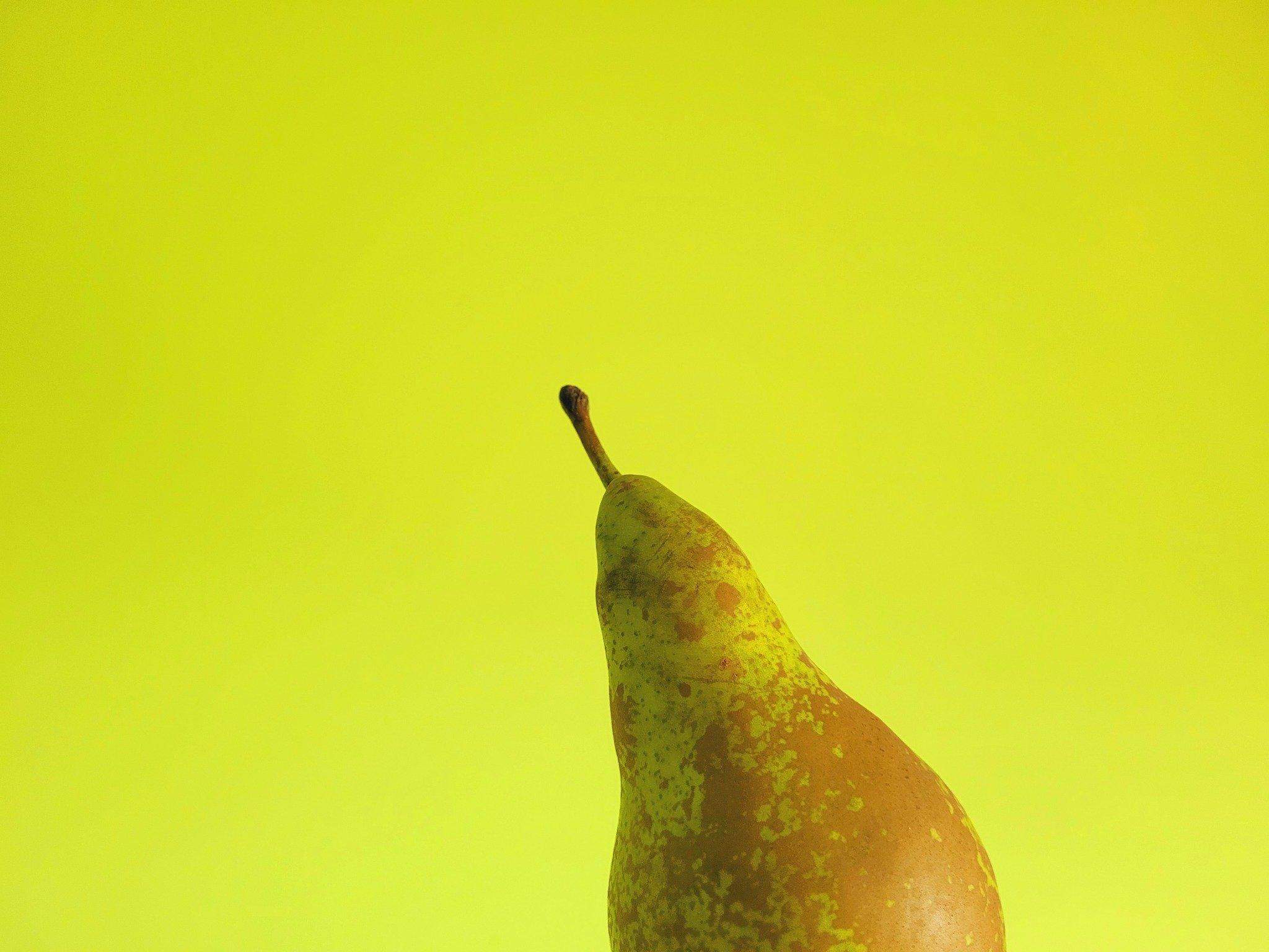 Dojrzała gruszka na tle intensywnie żółtego tła, przedstawiona w minimalistycznym ujęciu z mocnym kontrastem kolorów.